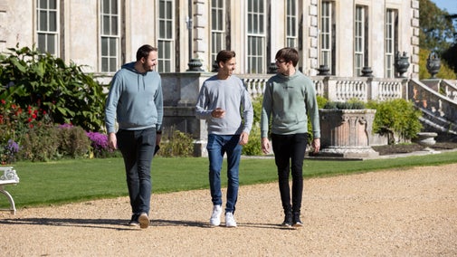 Friend group walking in the grounds of Kingston Lacy, Dorset on a gravel path with a building and flower border in the background